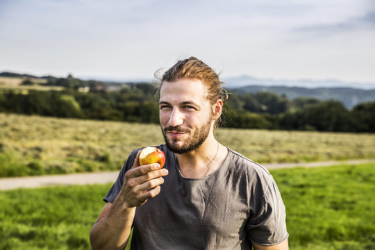 Young man eating an apple in rural landscape